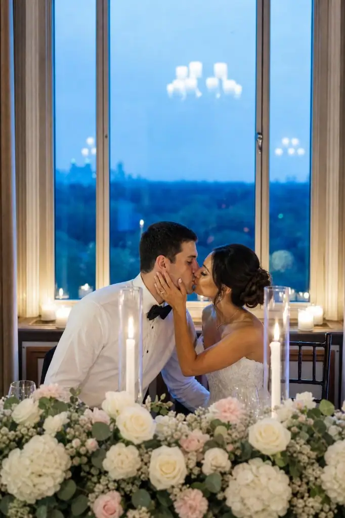 Bride and groom kissing at a candlelit sweetheart table with city twilight views